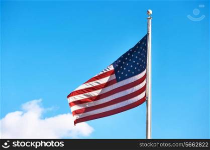 US American flag waving in the wind against blue sky and clouds