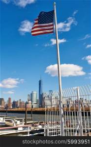 US American flag waving in the wind against blue sky with New York City Manhattan skyline at background