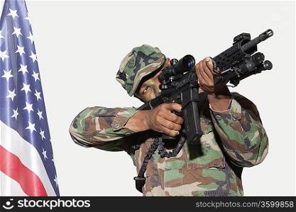US Marine Corps soldier aiming M4 assault rifle with American flag against gray background