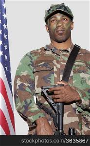 US Marine Corps soldier with M4 assault rifle standing by American flag over gray background