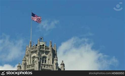 USA flag waving on the wind on the top of Chicago Tribune building. Flagstaff on the Golden Mile in Chicago city center. Cinematic american flag waving in the Windy City of Chicago.
