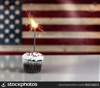 USA Independence Day celebration with decorated cupcake and glowing sparklers with flag in background 