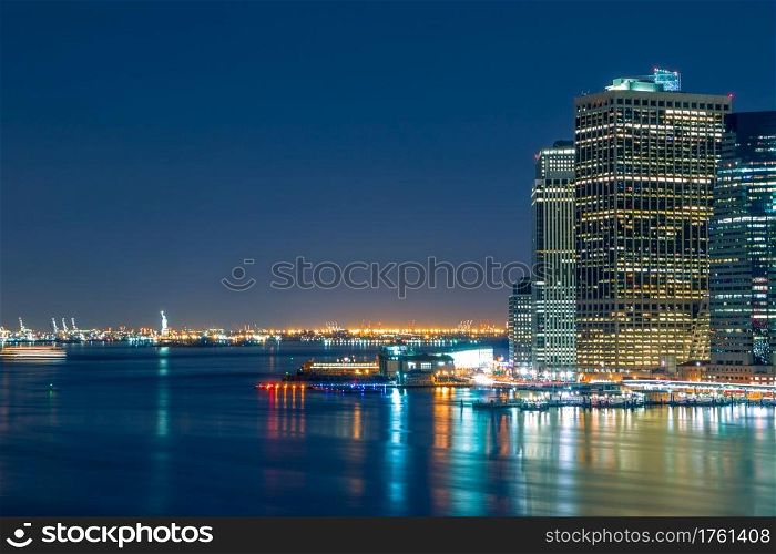 USA. New York City. Night lights of Manhattan waterfront and the Statue of Liberty on the horizon.