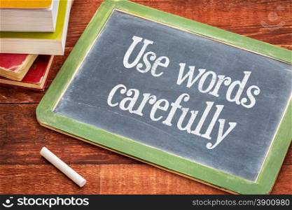 Use words carefully - text on a slate blackboard with a white chalk and a stack of books against rustic wooden table
