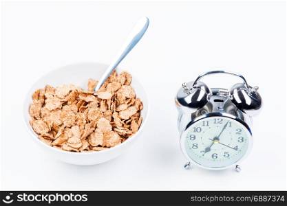 useful breakfast of cereal and alarm clock on white table close-up