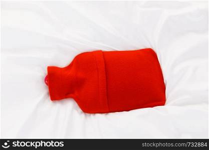 Useful things during fever concept. Warm red hot water bottle on white bedding. Warm red hot water bottle on white bedding