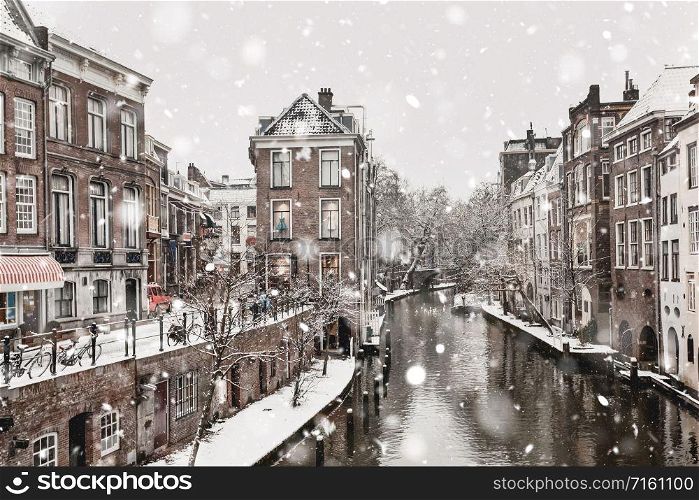 Utrecht The Netherlands in winter snowstorm. Historical buildings along canal in the city center in snowy weather. Magic Christmas mood. Monochromatic neutral tones with natural light