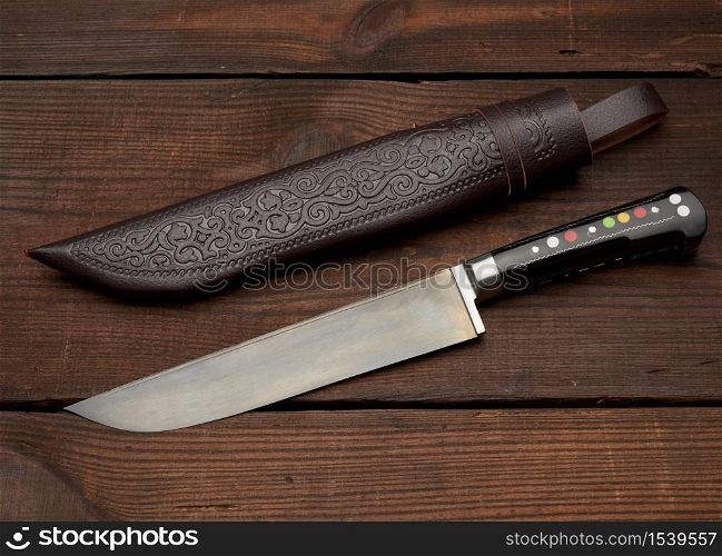 Uyghur Uzbek traditional universal sharp knife with a black handle on a brown wooden background, top view
