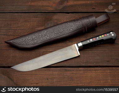 Uyghur Uzbek traditional universal sharp knife with a black handle on a brown wooden background, top view