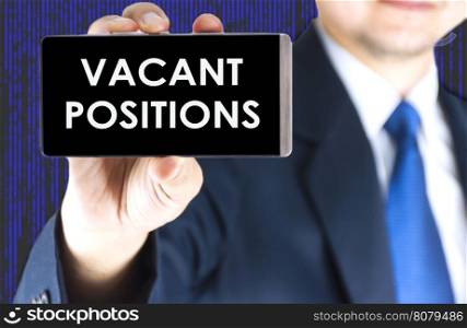 Vacant positions word on mobile phone screen in blurred young businessman hand and digital technology background