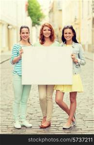 vacation, advertising and friendship concept - smiling teenage girls holding white blank billboard on city street
