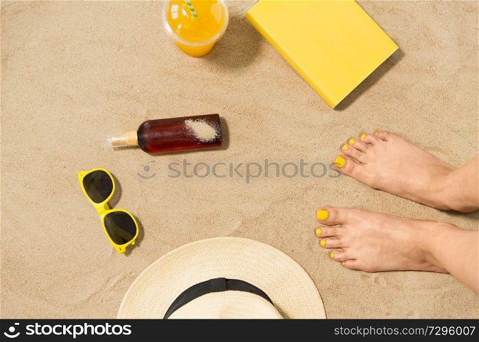vacation and summer holidays concept - female feet, sunglasses, straw hat, sunscreen and juice with book on beach sand. feet, hat, shades, sunscreen and juice on beach