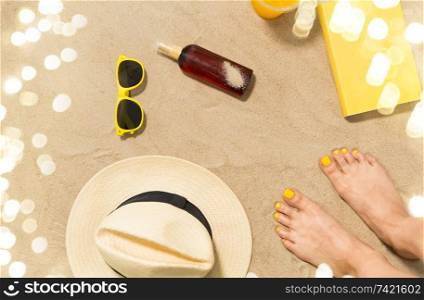 vacation and summer holidays concept - female feet, sunglasses, straw hat, sunscreen and book on beach sand. feet, hat, shades, sunscreen and book on beach