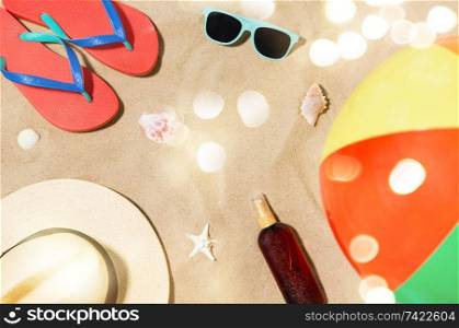 vacation and summer holidays concept - straw hat, flip flops, sunglasses, beach ball and sunscreen oil with seashells on sand. hat, flip flops and shades and beach ball on sand