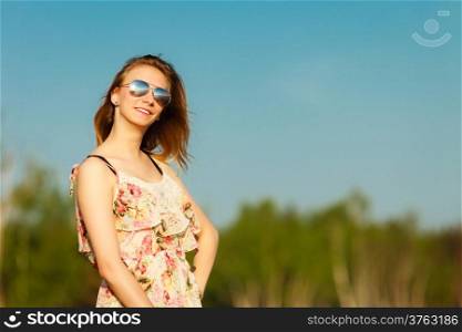 Vacation. Girl in summer dress and sunglasses standing on the empty beach. Young woman relaxing on the sea coast. Summertime.