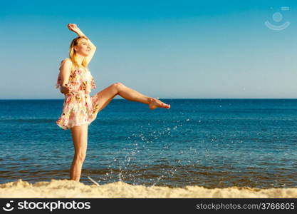 Vacation. Girl in summer dress splashing water on the coast. Young woman having fun relaxing on the sea. Summertime.