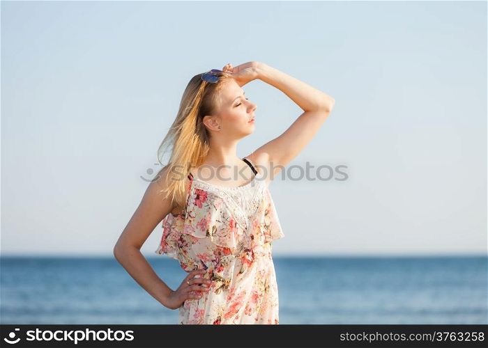 Vacation. Girl in summer dress standing alone on the empty beach. Young woman relaxing on the sea coast. Summertime.
