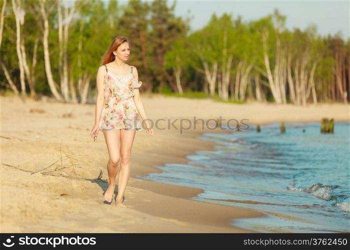 Vacation. Girl in summer dress walking alone on the empty beach. Young woman relaxing on the sea coast. Summertime.