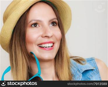 Vacation. Happy girl in summer clothes blue sunglasses and straw hat. Portrait of smiling woman tourist on gray.