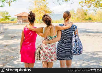 Vacation holiday back rear view of group three female woman girl friends hug hugging while walking in autumn or summer on the rest area by the road during travel