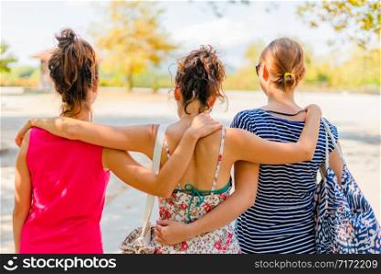 Vacation holiday back rear view of group three female woman girl friends hug hugging while walking in autumn or summer on the rest area by the road during travel