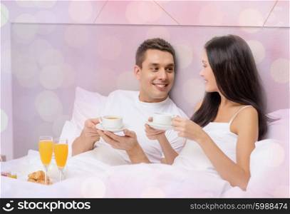 vacation, holidays, people, romance and valentines day concept - happy couple having breakfast in bed at hotel or home over lights background