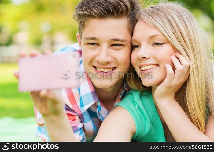 vacation, holidays, technology and friendship concept - smiling couple lying on blanket and making selfie with smartphone in park
