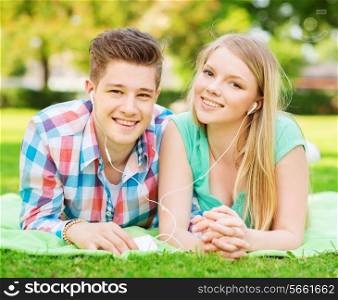 vacation, holidays, technology and friendship concept - smiling couple with smartphone and earphones lying on blanket in park