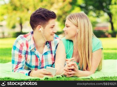 vacation, holidays, technology and friendship concept - smiling couple with smartphone and earphones lying on blanket in park