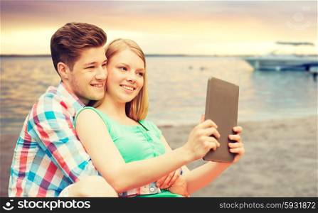 vacation, holidays, travel, technology and love concept - smiling couple with tablet pc computer taking selfie over sunset beach background
