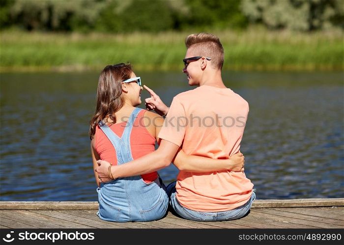 vacation, love and people concept - happy teenage couple sitting and hugging on river berth at summer