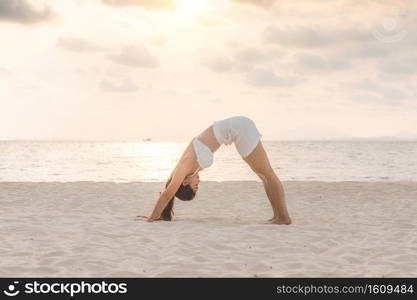 Vacation of Attractive Asian woman relaxing in yoga Downward Facing dog or Adho Mukha Svanasana pose on sand and beach with sunset sea in Thailand Tropical island,Feel comfortable and relax in holiday