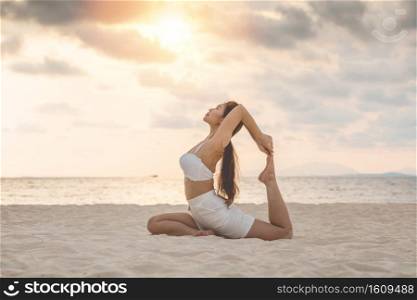 Vacation of Attractive Asian woman relaxing in yoga king pigeon pose on the sand and beach with sunset beautiful sea in Tropical island,Feeling comfortable and relax in holiday,Vacations Concept