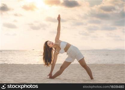 Vacation of Attractive Asian woman relaxing in yoga Triangle pose on the sand and beach with sunset beautiful sea in Tropical island,Feeling comfortable and relax in holiday,Vacations Concept