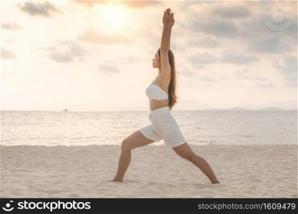 Vacation of Attractive Asian woman relaxing in yoga Warrior one pose on the sand and beach with sunset beautiful sea in Tropical island,Feeling comfortable and relax in holiday,Vacations Concept