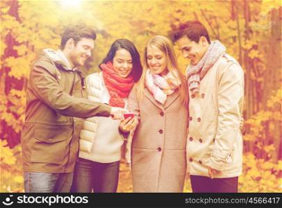 vacation, people, technology and friendship concept - group of smiling friends with smartphone in autumn park