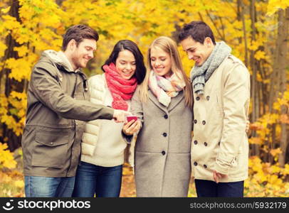 vacation, people, technology and friendship concept - group of smiling friends with smartphone in autumn park