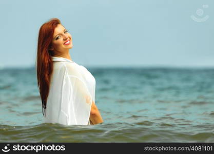 Vacation. Sensual girl wet cloth in water on the coast. Redhair woman having fun relaxing on the sea. Summertime.