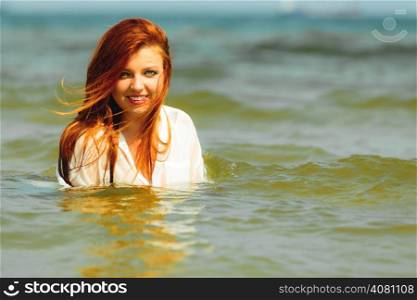 Vacation. Sensual girl wet cloth in water on the coast. Redhair woman having fun relaxing on the sea. Summertime.