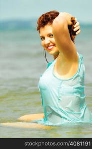 Vacation. Sensual girl wet cloth in water on the coast. Redhair woman having fun relaxing on the sea. Summertime.