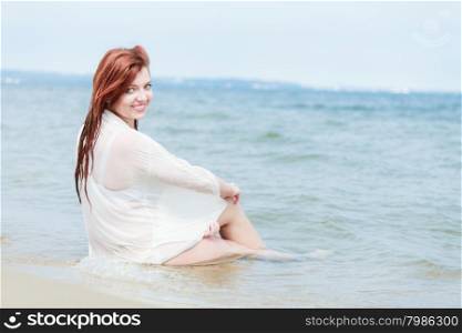 Vacation. Sensual girl wet cloth in water on the coast. Redhair woman having fun relaxing on the sea. Summertime.
