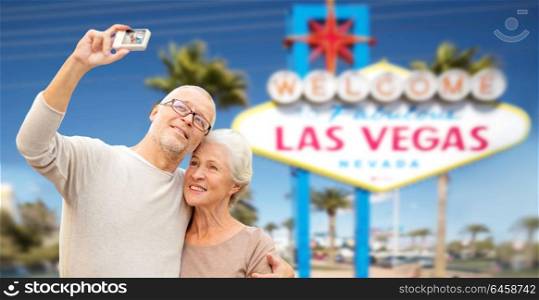 vacation, tourism and travel concept - happy senior couple hugging and taking photo by digital camera over welcome to fabulous las vegas sign background. senior couple taking selfie by camera at las vegas