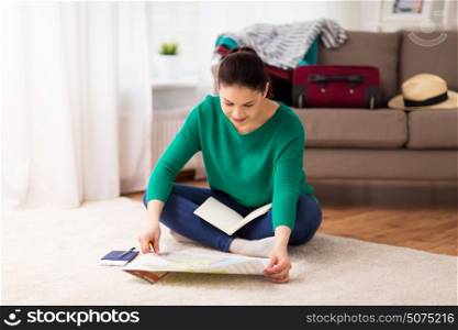 vacation, tourism, travel and people concept - happy young woman with map, notebook and passport at home going on trip. woman with map planning her travel at home