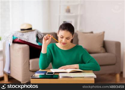 vacation, tourism, travel and people concept - happy young woman with notebook, gadgets and map at home going on trip