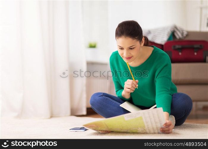 vacation, tourism, travel and people concept - happy young woman with notebook, passport and map at home going on trip