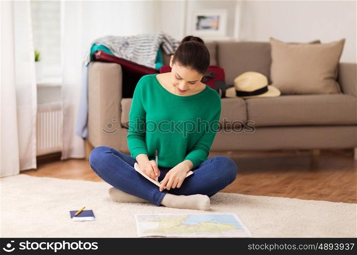 vacation, tourism, travel and people concept - happy young woman with notebook, passport and map at home going on trip