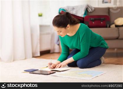 vacation, tourism, travel and people concept - happy young woman with notebook, gadgets and map at going on trip. woman with notebook and travel map at home