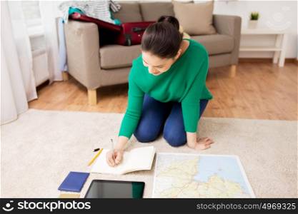 vacation, tourism, travel and people concept - happy young woman with notebook, gadgets and map at going on trip. woman with notebook and travel map at home