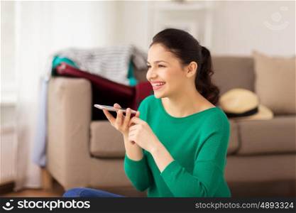 vacation, tourism, travel and people concept - happy young woman with smartphone using voice command recorder at home