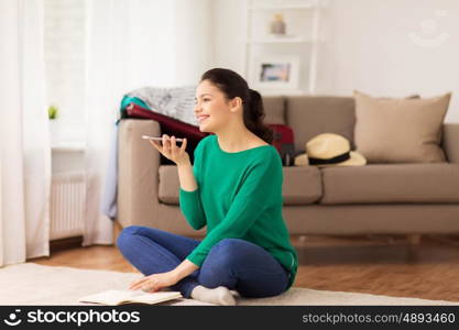 vacation, tourism, travel and people concept - happy young woman with smartphone using voice command recorder at home